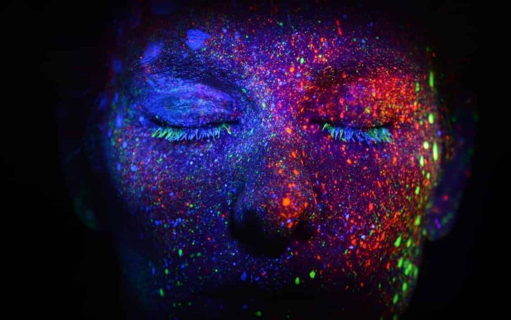 A person with glow paint on his face showing How To Charge Glow In The Dark Paint